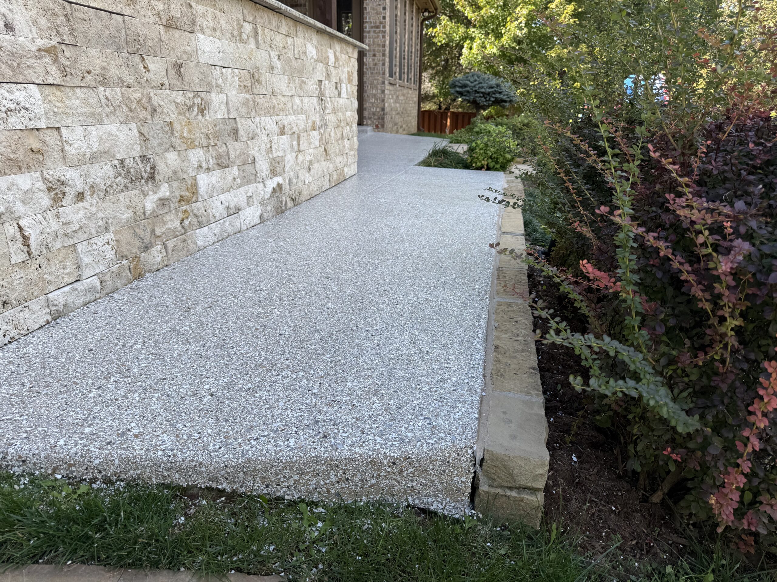 Polyaspartic flake coating on exterior concrete walkway beside stone wall