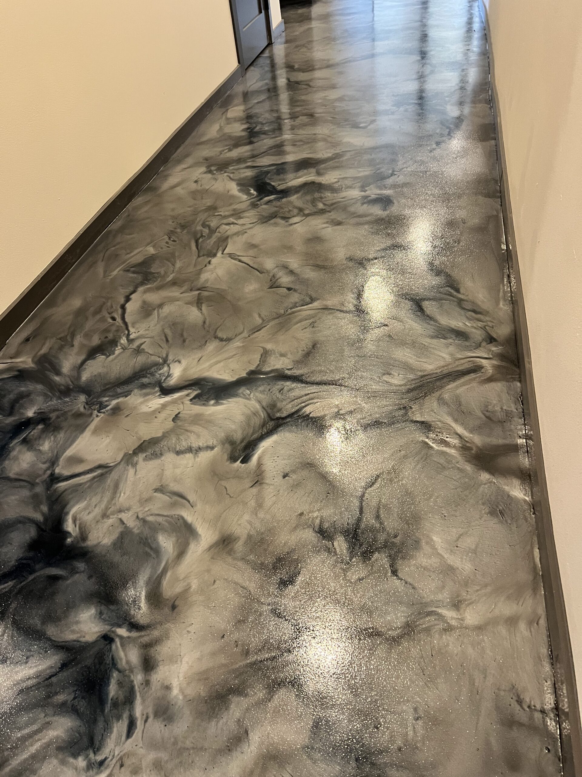 Metallic epoxy floor coating with flowing grey and black pattern in interior hallway